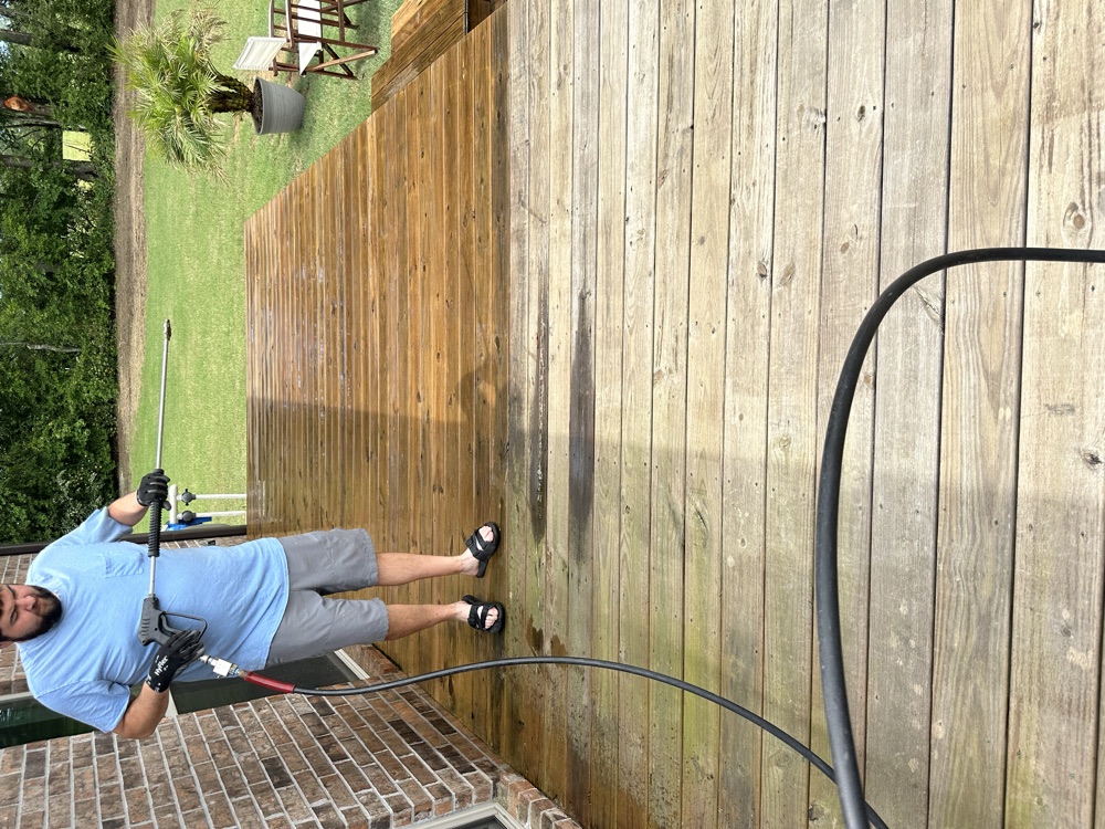 Seth pressure washing a wood deck, clean boards next to gray weathered ones