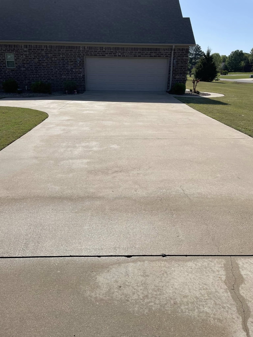 Bright, freshly cleaned concrete driveway in front of a brick garage
